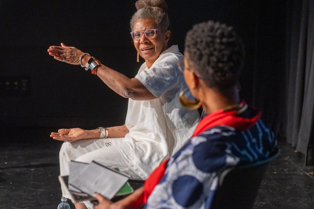 M.NourbeSe Philip points with an open hand during a discussion.